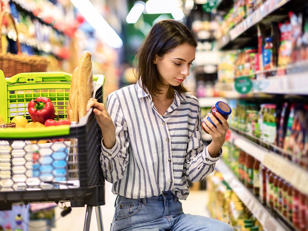 Woman checking expiry date on a bottle in grocery aisle.