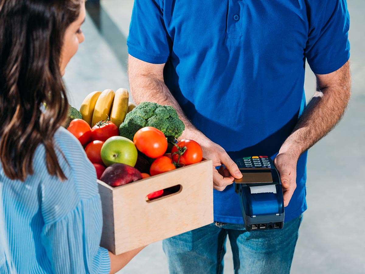 Person tapping to pay for box of vegetables on a POS.