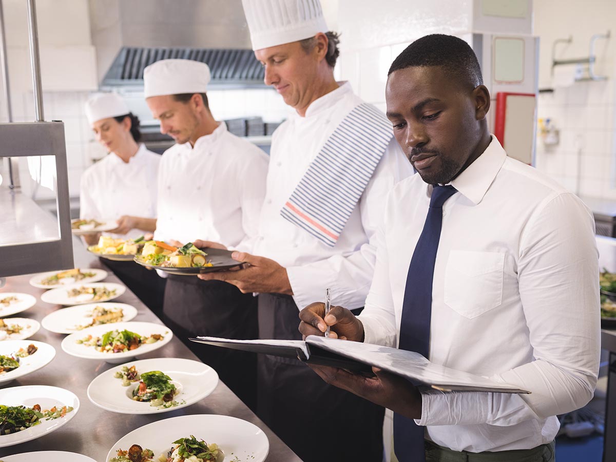 Restaurant manager looking at books as three chefs prepare food.