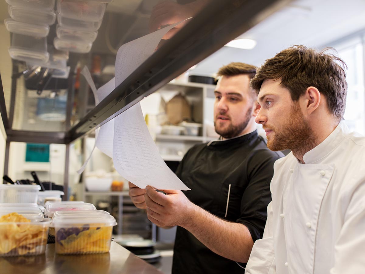 Two chefs looking at food inventory sheet.