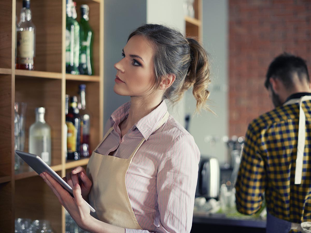 Bartender on tablet checking alchol inventory at restaurant.