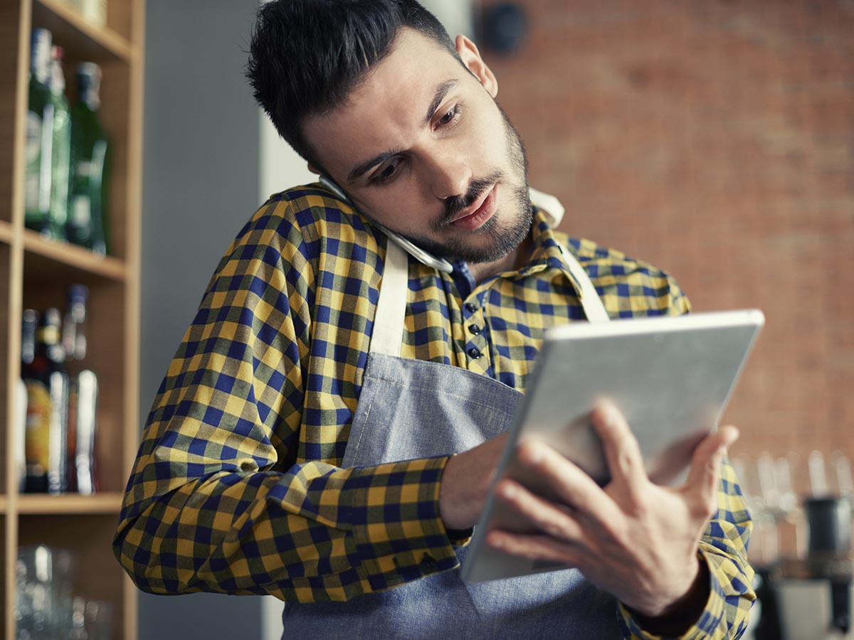 Restaurant owner on the phone while holding a tablet as well.