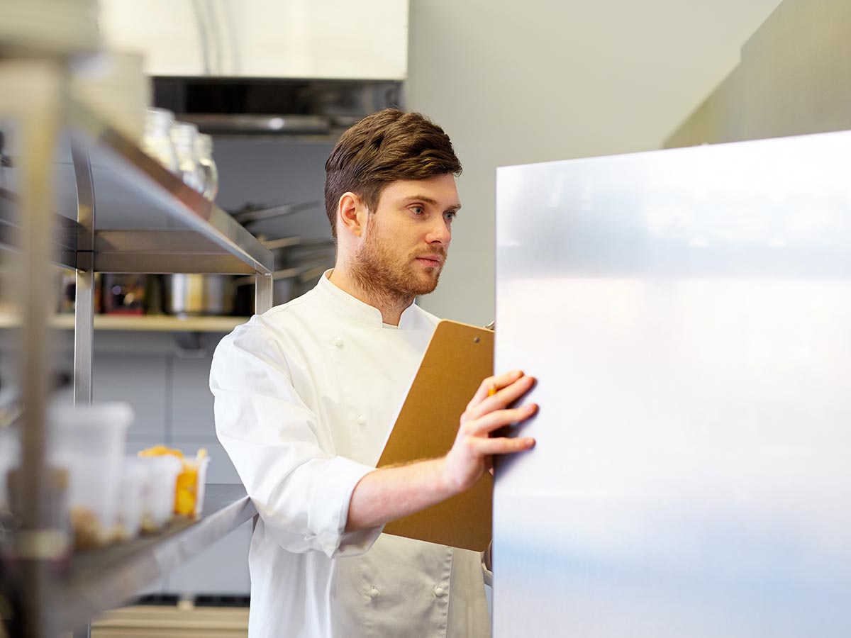 Restaurant Chef looking in fridge with a clipboard for inventory.
