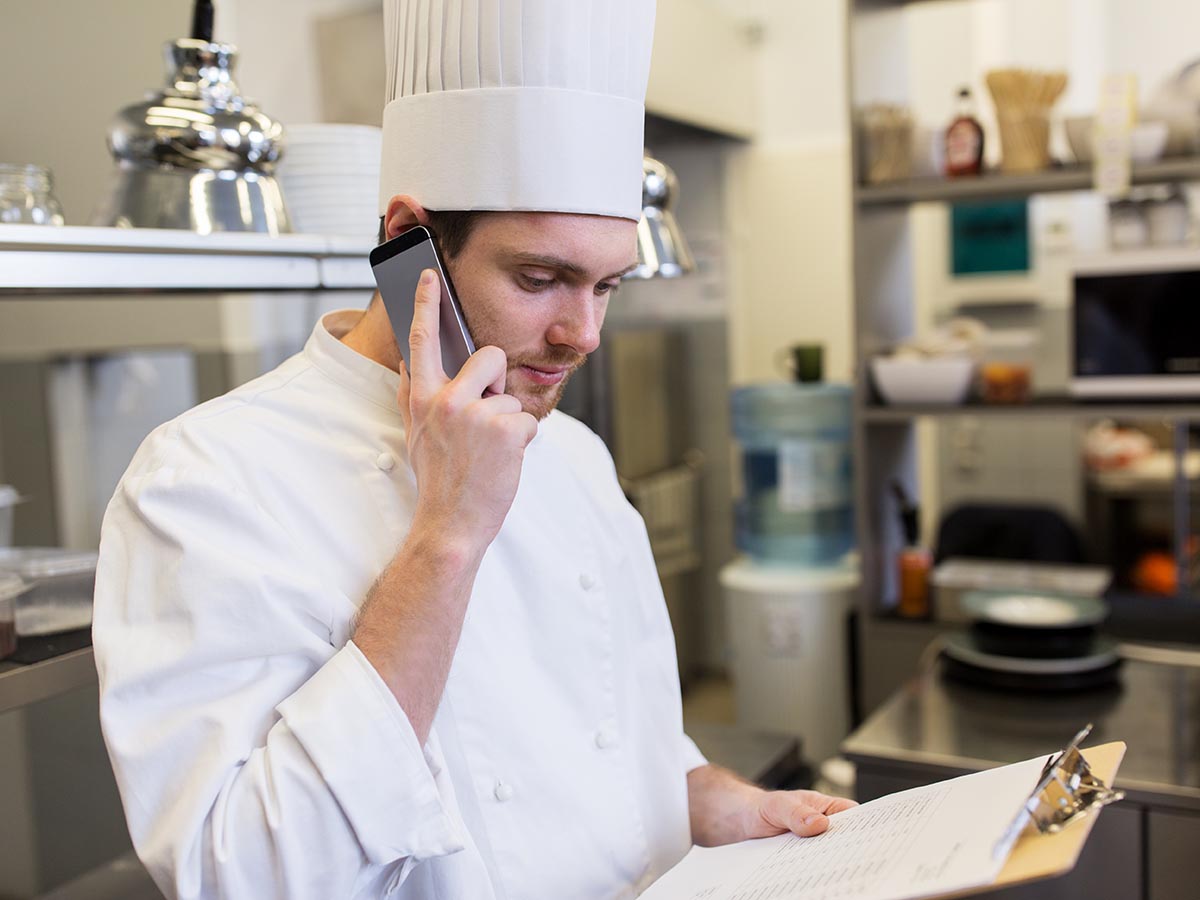 Restaurant Chef on the phone speaking to supplier while holding clipboard.