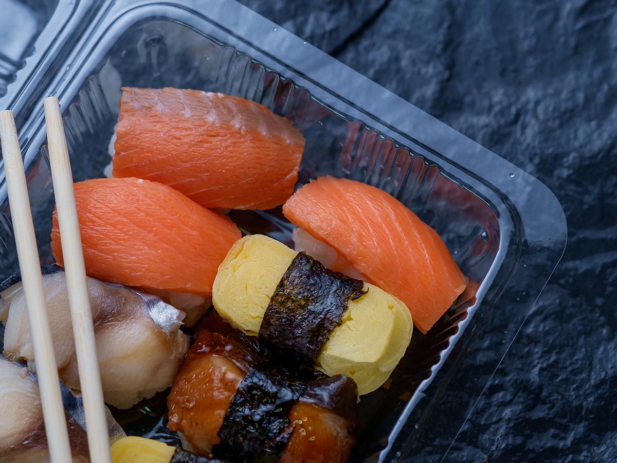 Sushi in a clear takeout container with chopsticks.