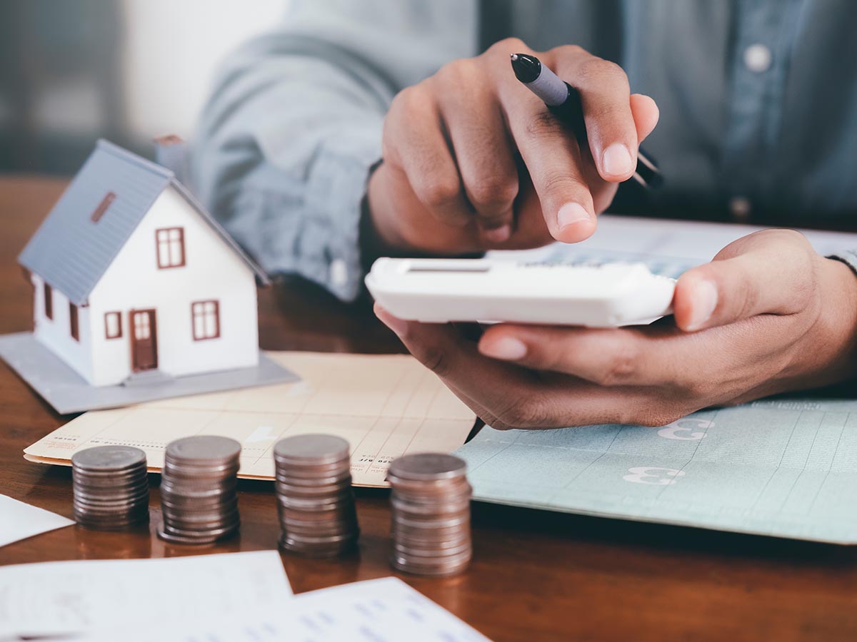 Hands holding pen and calculator next to papers and stacks of coins.