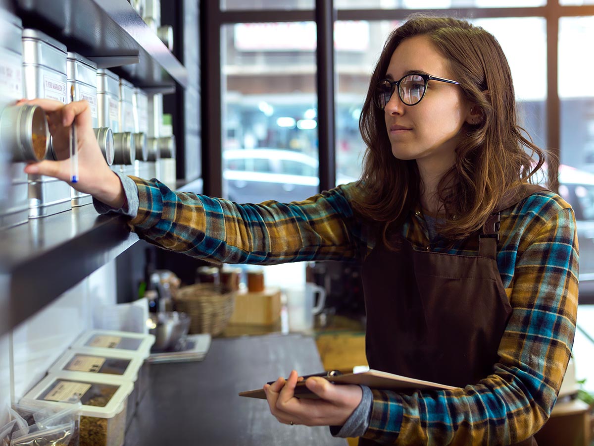 Young woman with clipboard checks inventory of tea store.
