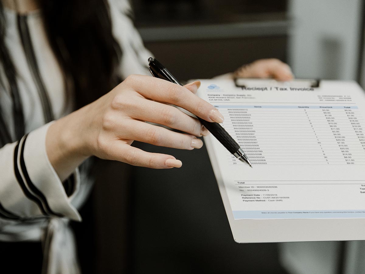 Woman's hand is holding a pen and passing an invoice on a clipboard.