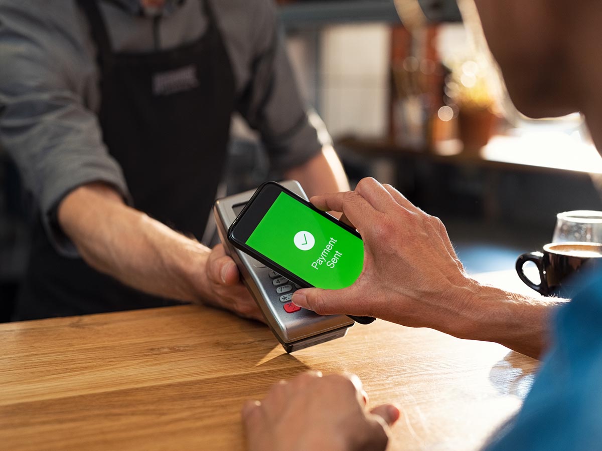 Customer tapping phone on payment system, screen display shows payment sent.