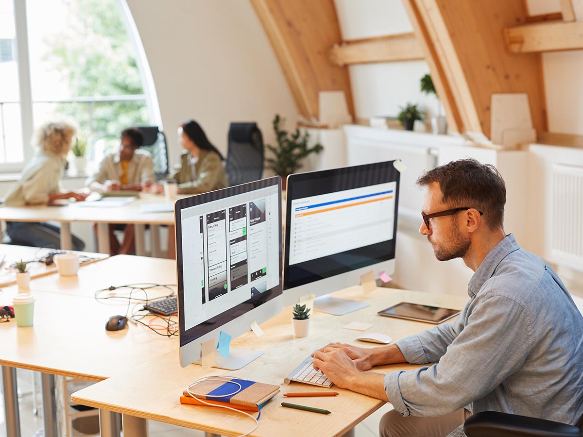 Man with glasses working on two computer screens.