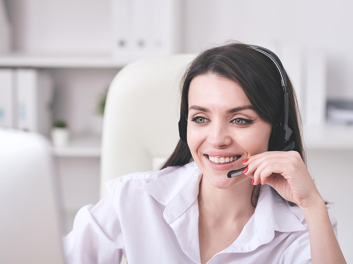 Young woman smiles while talking on phone support head set.