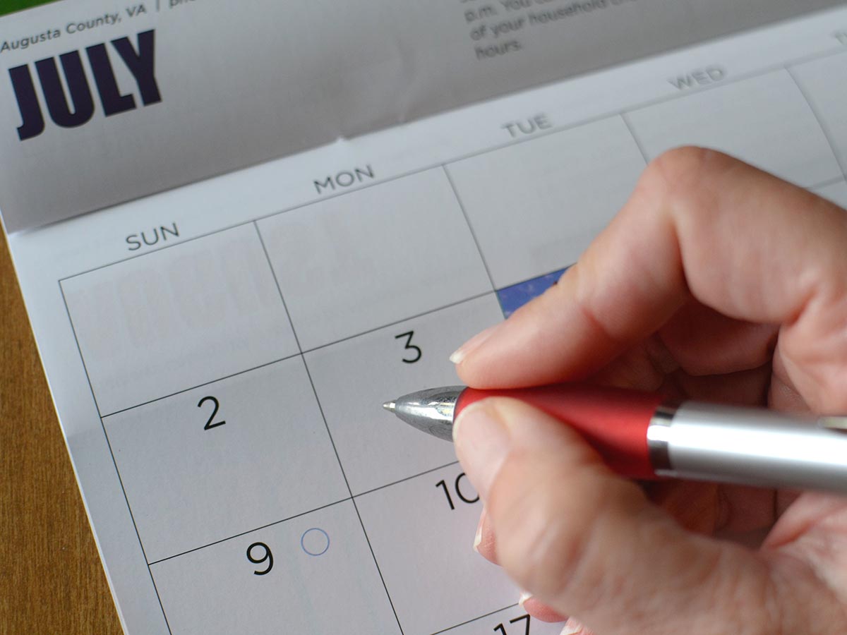 Hand holding a pen over a calendar.